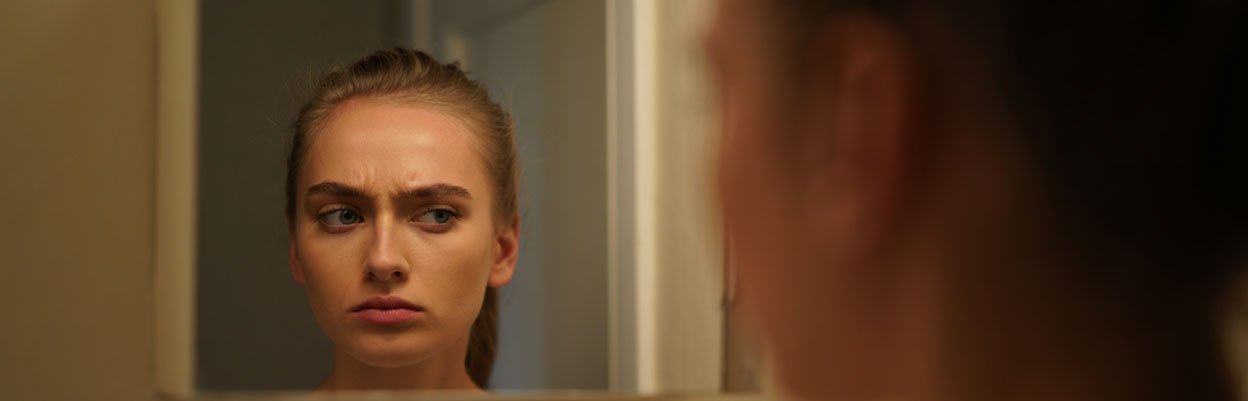 Девушка с не довольствием смотрит в отражение с зеркалом